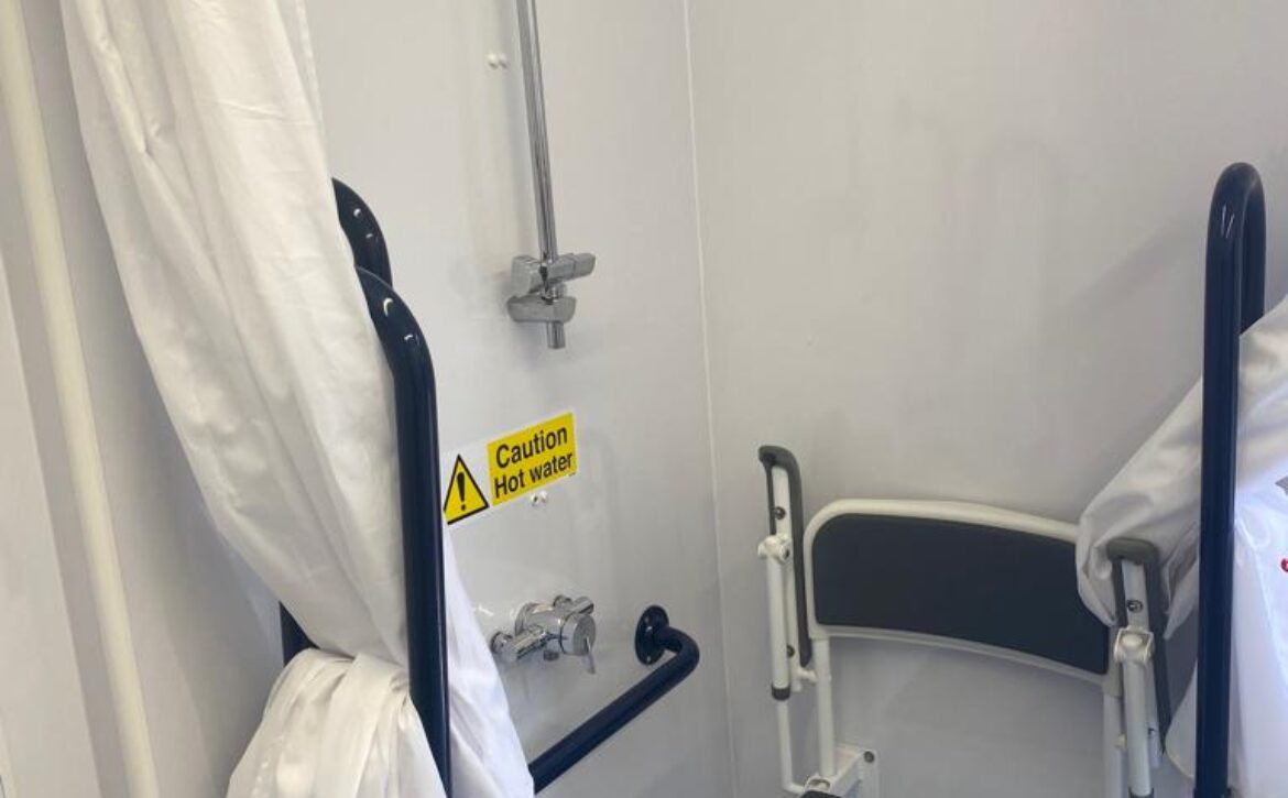 Picture of the accessible shower, with wet room floor, hand rails and shower chair