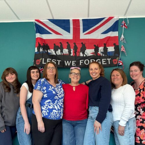 Team Pic 3 Photo of the KW Therapy team standing in front of the Union Jack flag emblazoned with silhouettes of soldiers and the words 'Lest We Forget'