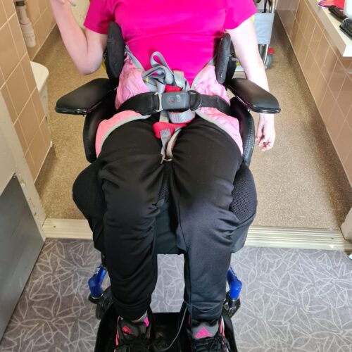 Loren photo wheelchair Client sat in a powerchair with lap belt and cushions for posture support